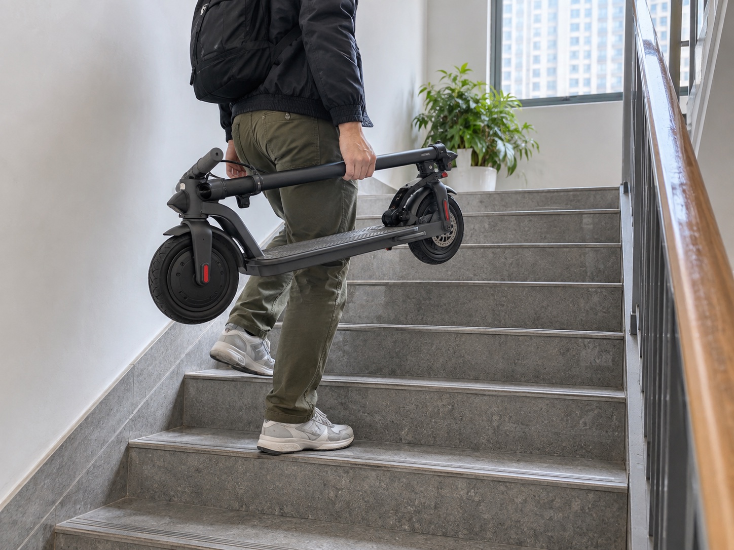 Commuter carrying a folded scooter on indoor stairs